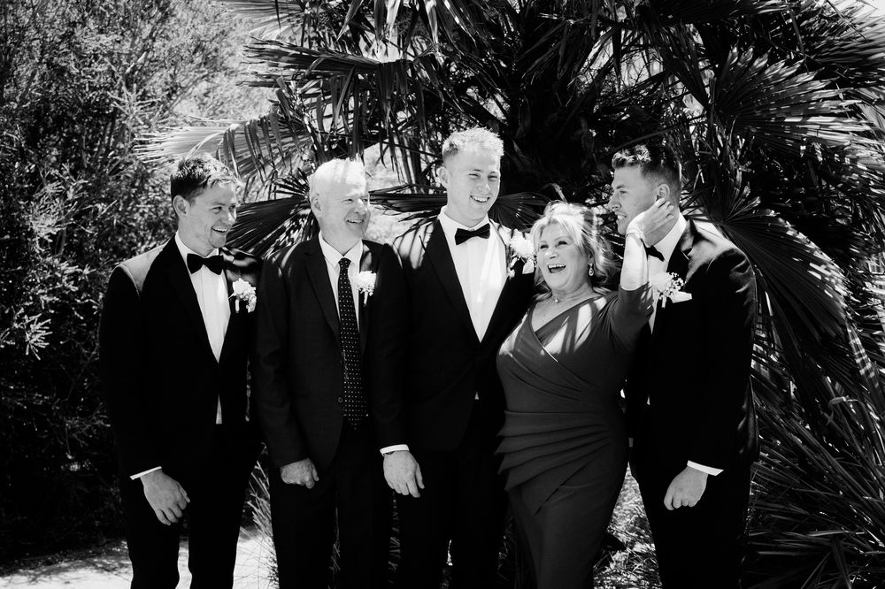 Wedding party shares a candid moment in front of palm trees in formal attire.