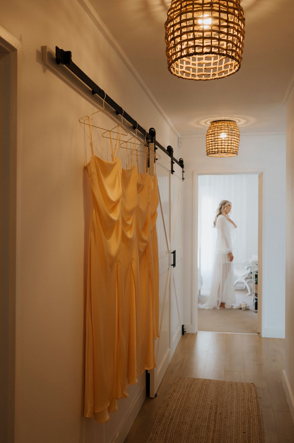Yellow bridesmaid dresses hanging in hallway with elegant lighting and bridal reflection.