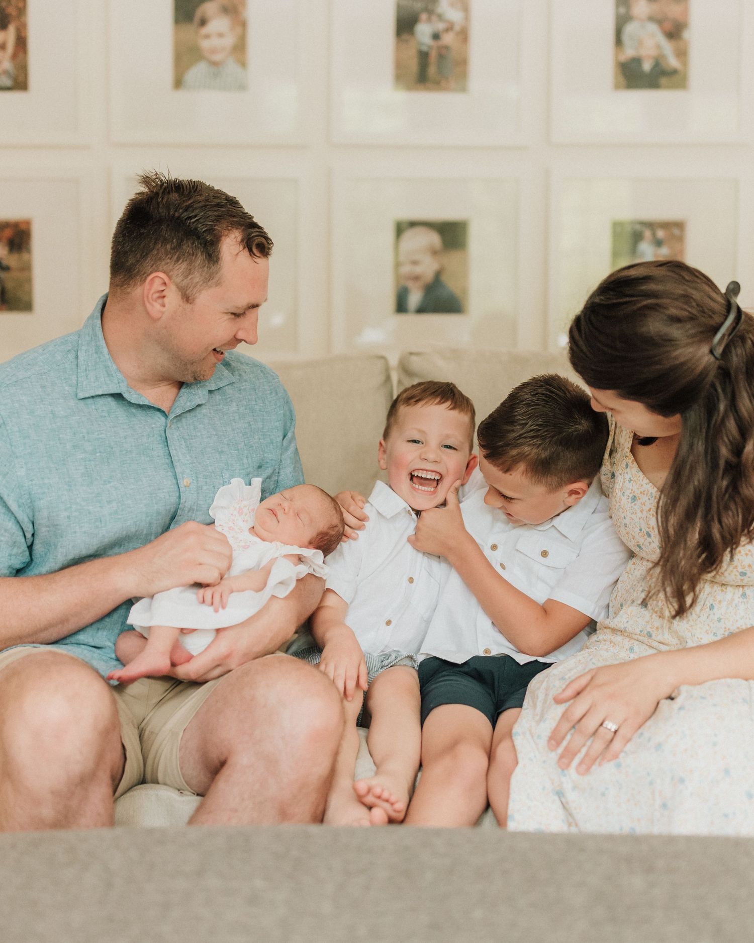 A happy family gathers on a couch to welcome their new baby while framed photos decorate the wall.