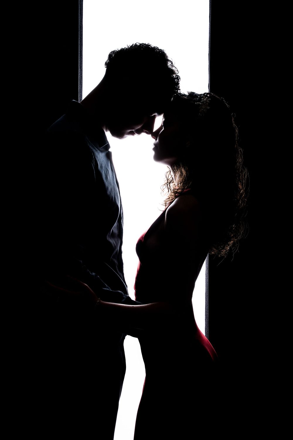 Dramatic silhouette of a romantic couple in intimate pose against bright backlighting.