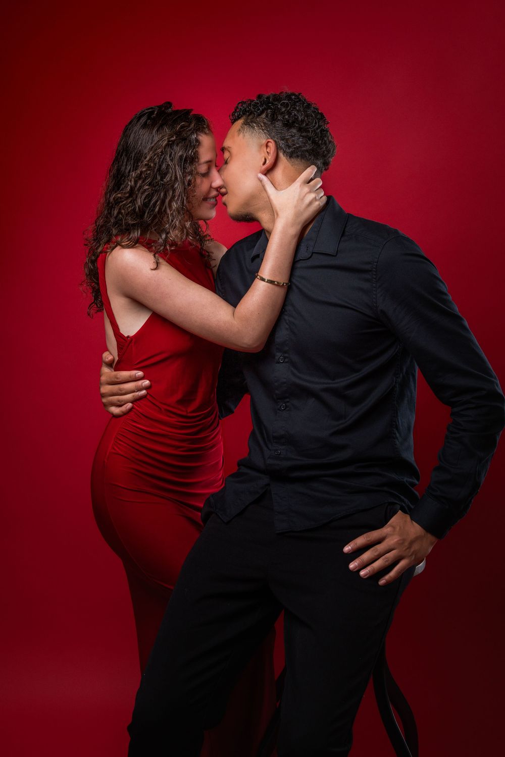 Couple in contrasting black and red outfits share intimate moment against crimson background.