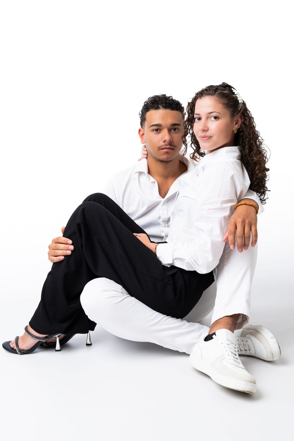 Stylish couple in contrasting black and white outfits posing together on light background.