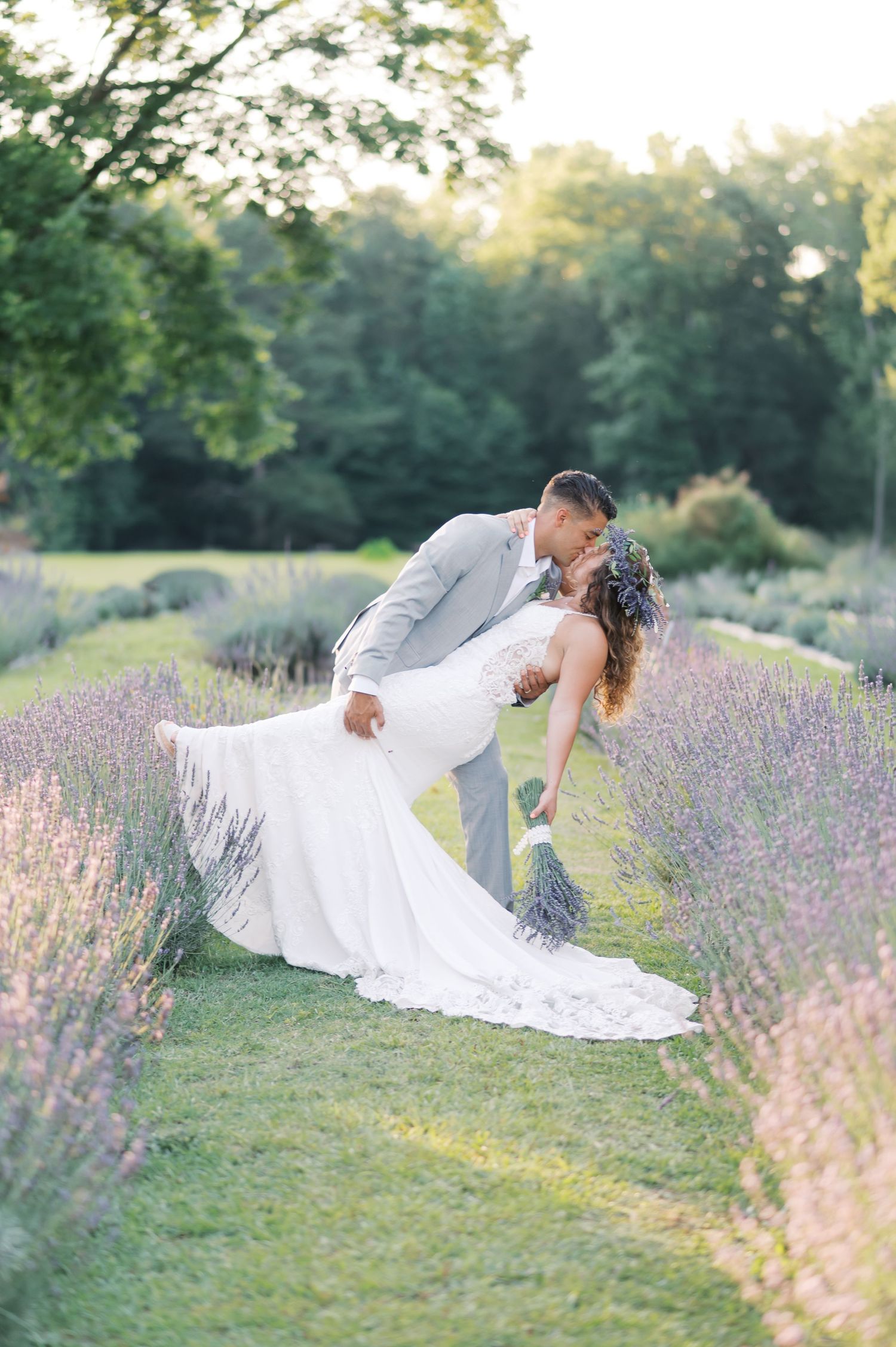 A romantic wedding photo shows a couple sharing a dip kiss in a blooming lavender field during golden hour.
