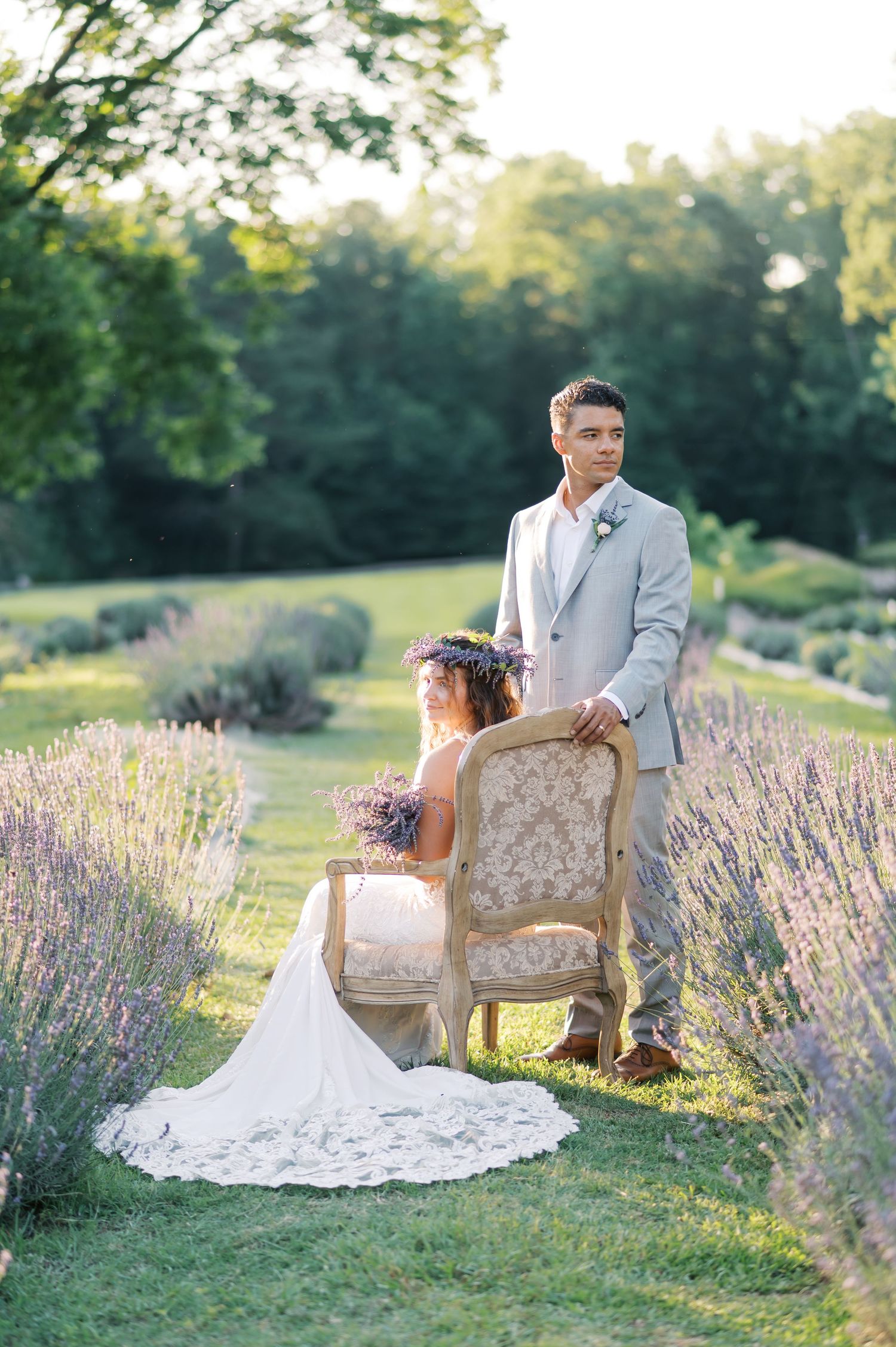 A romantic wedding photo in a lavender field with a vintage chair and golden evening sunlight filtering through trees.