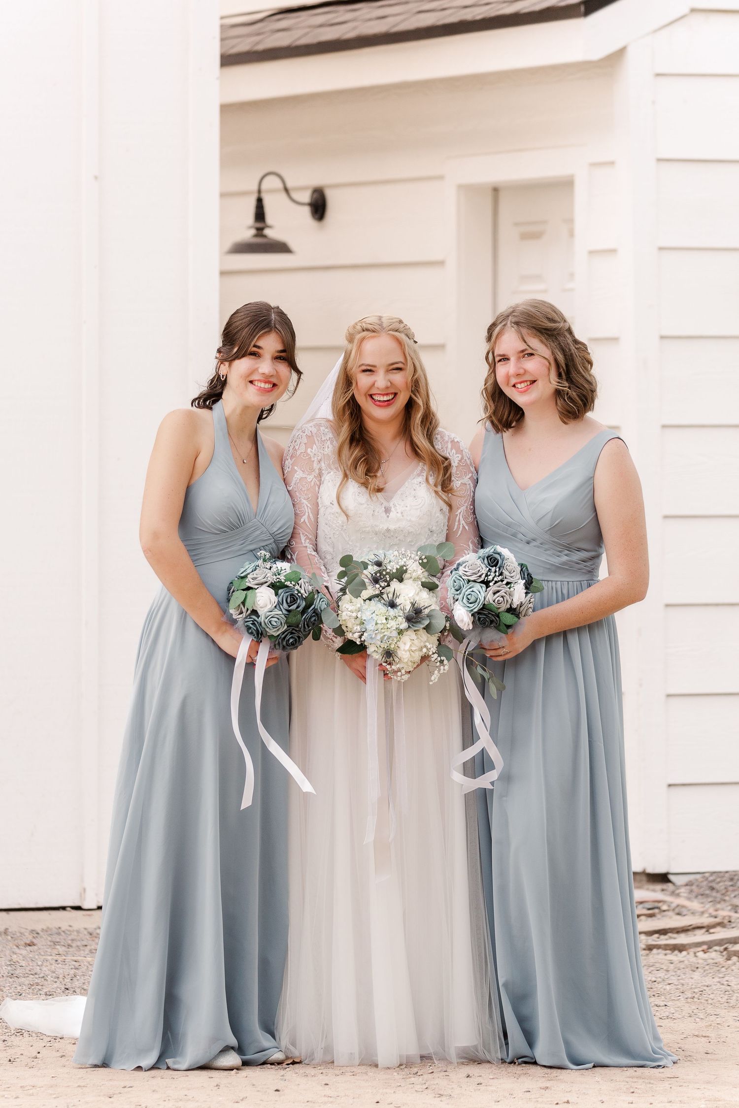 Bridesmaids wearing dusty blue gowns gather around with floral bouquets for photos.