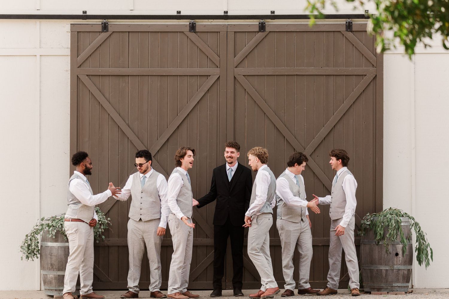 Wedding party in gray suits lined up against rustic barn doors for creative photo.