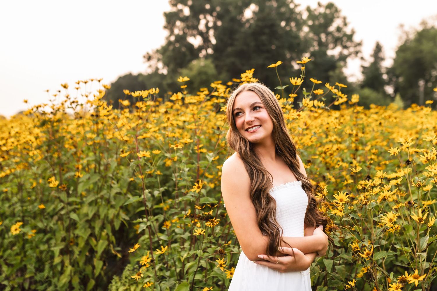 Golden Hour portrait of a senior girl leaning on a white fence with the sun glowing on the field behind her.