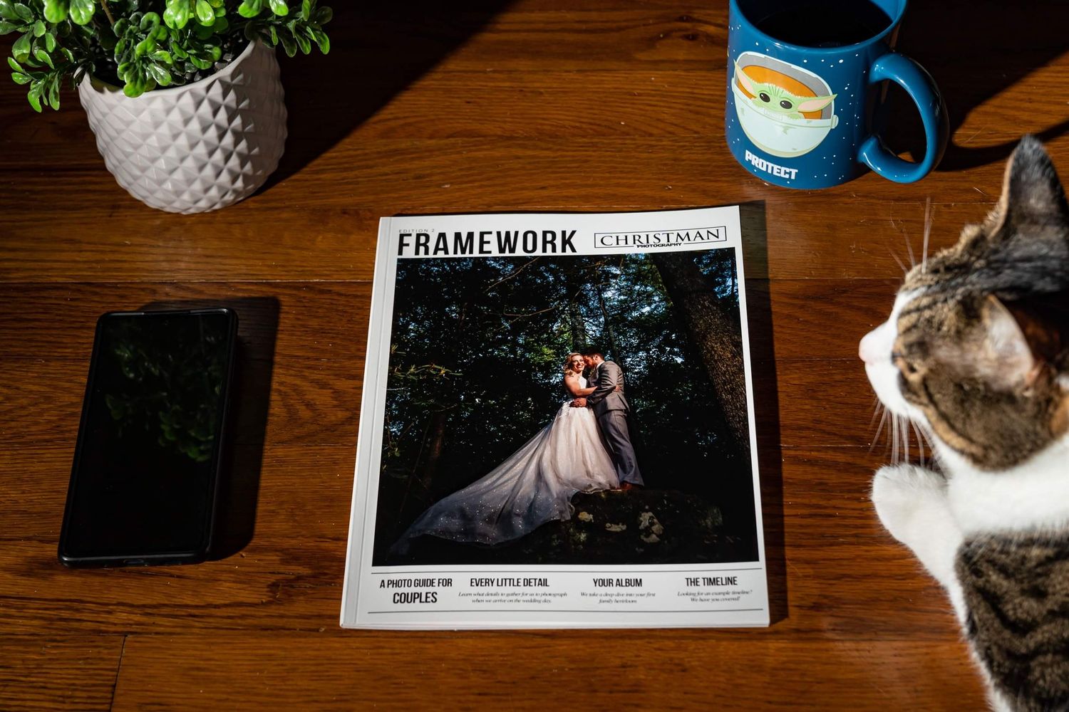 Wedding details and magazines arranged on a wooden table with a blue coffee mug.
