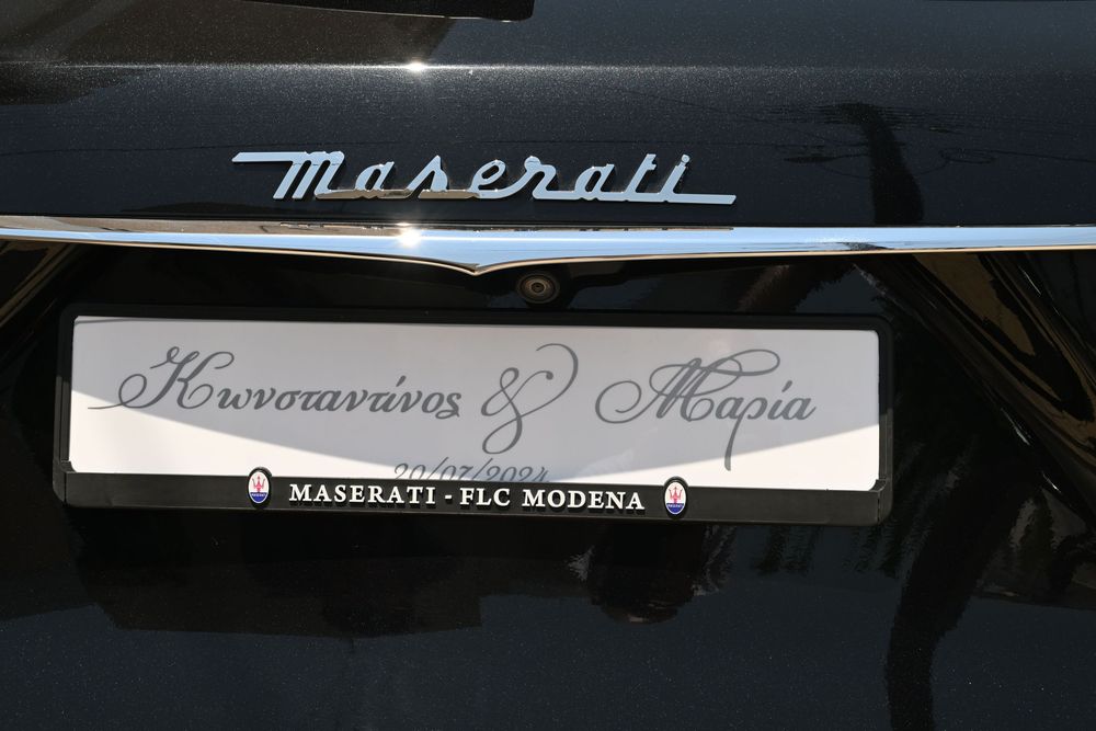 Close-up of Maserati script badge and dealership plate on black vehicle.