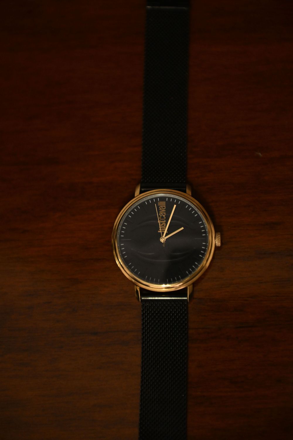 Elegant black and gold wristwatch with mesh band displayed on dark wooden surface.