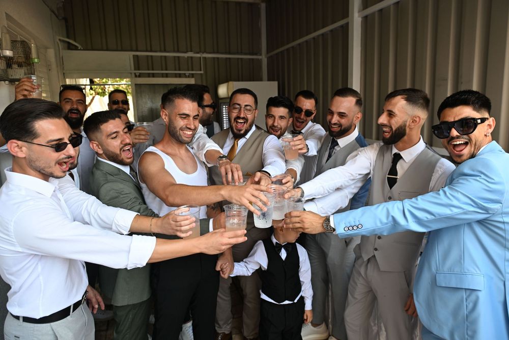 Group of groomsmen in suits joining hands in celebratory circle.