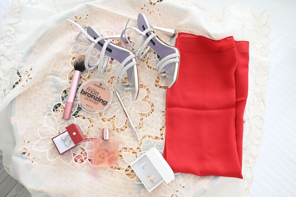 Silver wedding shoes and a red garment lay elegantly arranged with decorative confetti and tags.