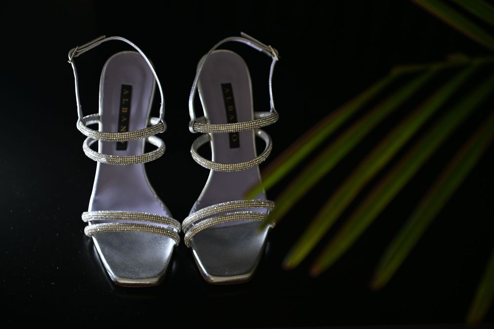 Elegant silver strappy wedding sandals photographed against a dark background with palm leaves.