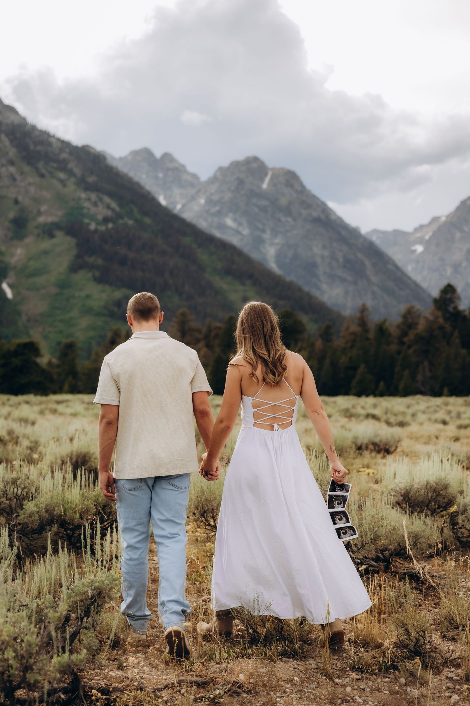 A pair strolls through sage brush meadows beneath towering mountain peaks in Grand Teton National Park.