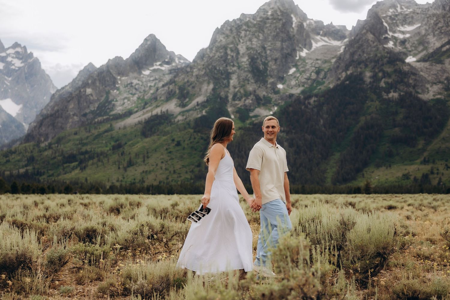 Romantic couple standing in field of sagebrush with majestic Teton mountain range backdrop.
