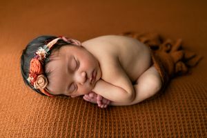 Orlando FL Newborn Photography 21 Moments Photography newborn girl sleeping on orange backdrop wearing floral headband