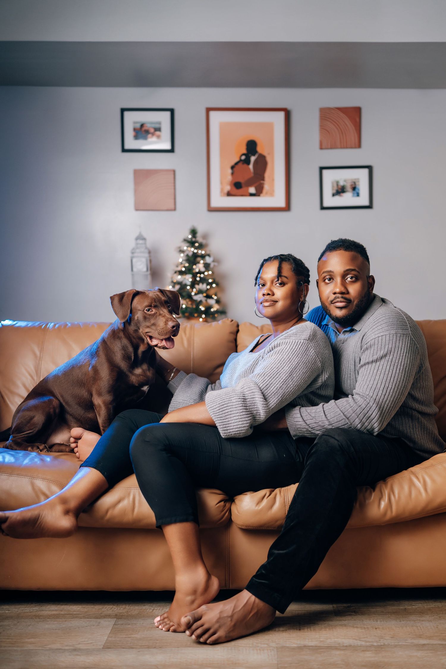 Group sitting together on brown leather couch with holiday decor and frames visible on wall in background.
