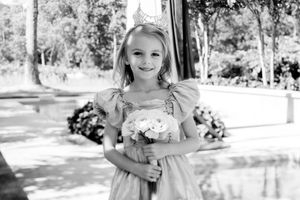 Black and white portrait of a bridesmaid in a light dress holding a bouquet of white flowers in an outdoor garden setting.