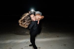 A silhouetted couple performs a dramatic dance dip under dramatic lighting in a dark space.