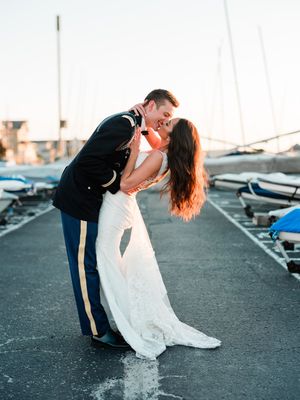 Wedding couple performs romantic dip pose against boats and marina backdrop in soft lighting.