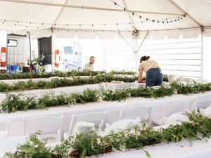 Long banquet tables under a white tent are decorated with lush greenery garlands for an outdoor wedding reception.