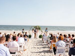 A peaceful beach wedding ceremony setup with white chairs facing the ocean as guests gather on the sandy shore.