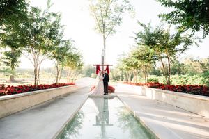 Couple standing on pathway with reflecting pool surrounded by trees at sunset.