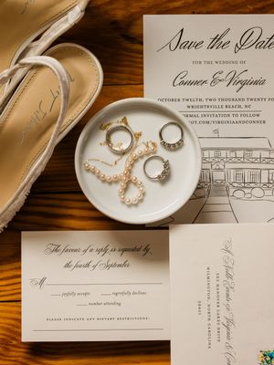 A collection of wedding invitation stationery and rings photographed on a wooden surface in warm lighting.