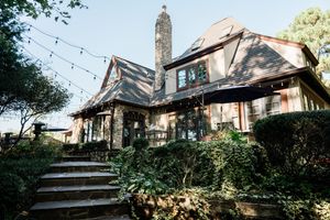 A cozy stone cottage with wooden features surrounded by lush greenery and gardens on a scenic hillside property.