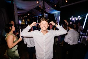 A cheerful guest dances with raised arms during a nighttime party under twinkle lights and draped fabric decor.
