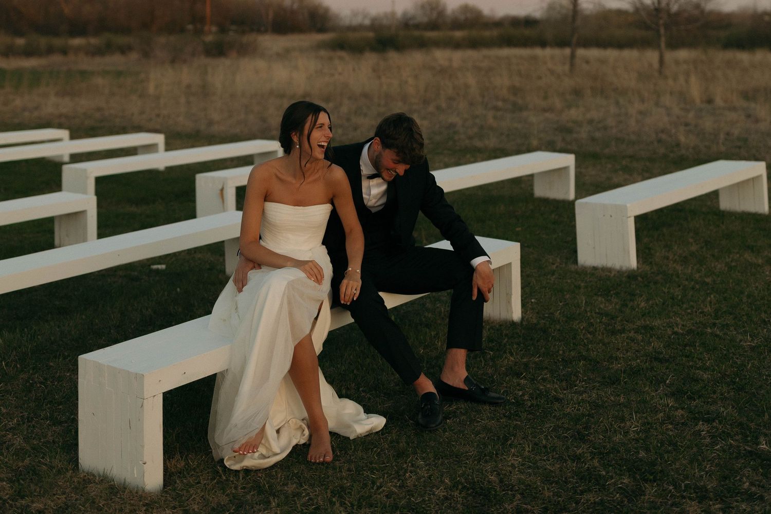 Couple sharing an intimate moment on white benches during sunset at their wedding venue.