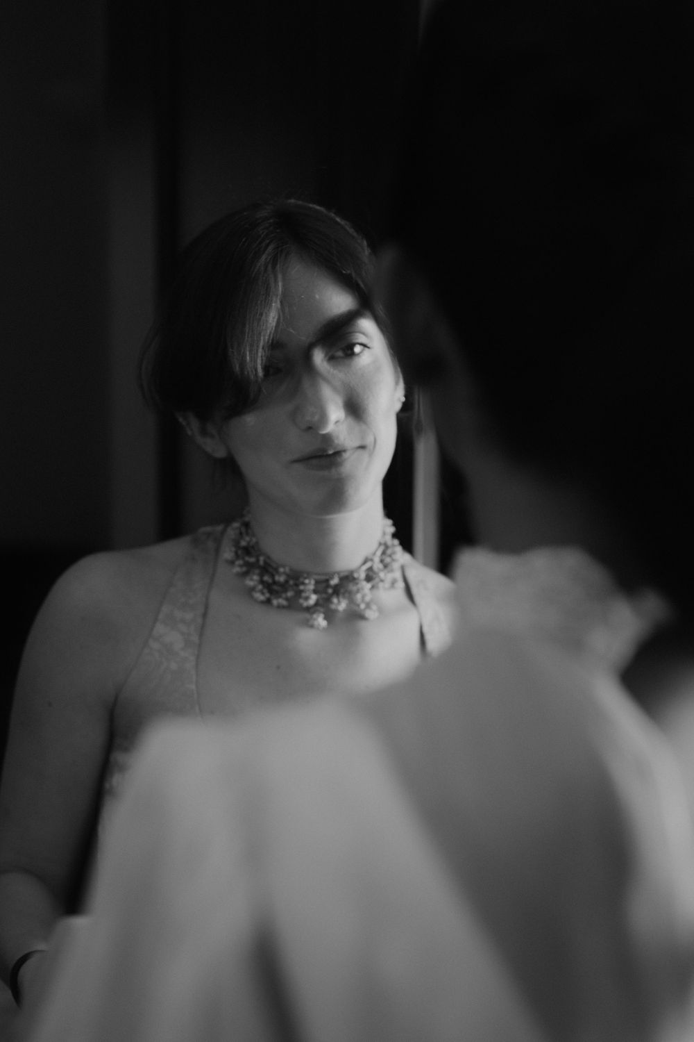 Close-up artistic black and white portrait with dramatic lighting and a statement necklace.