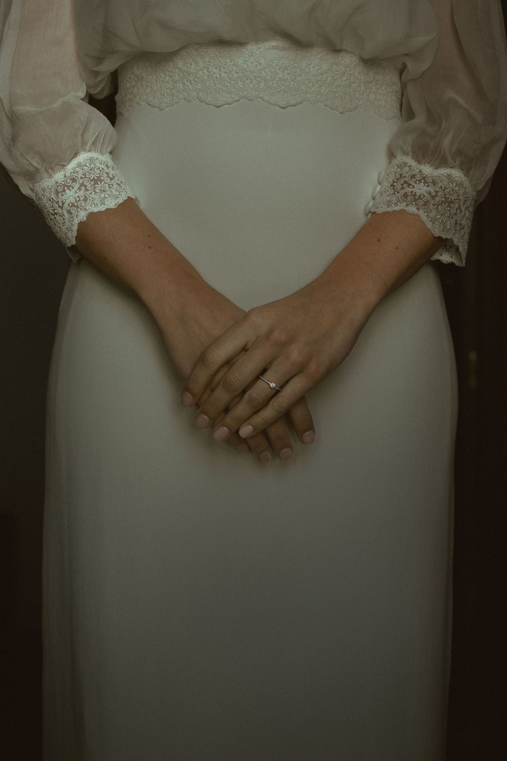 Close-up shot of hands with a wedding ring against a white lace wedding dress.