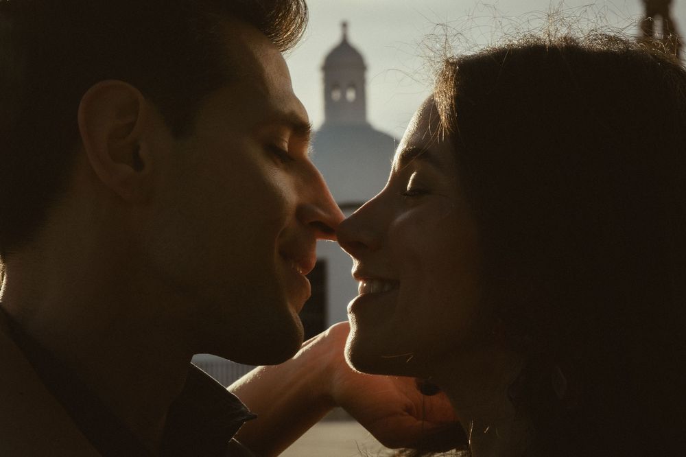 A romantic silhouette of a couple about to kiss with a church steeple visible in the warm backlit background.