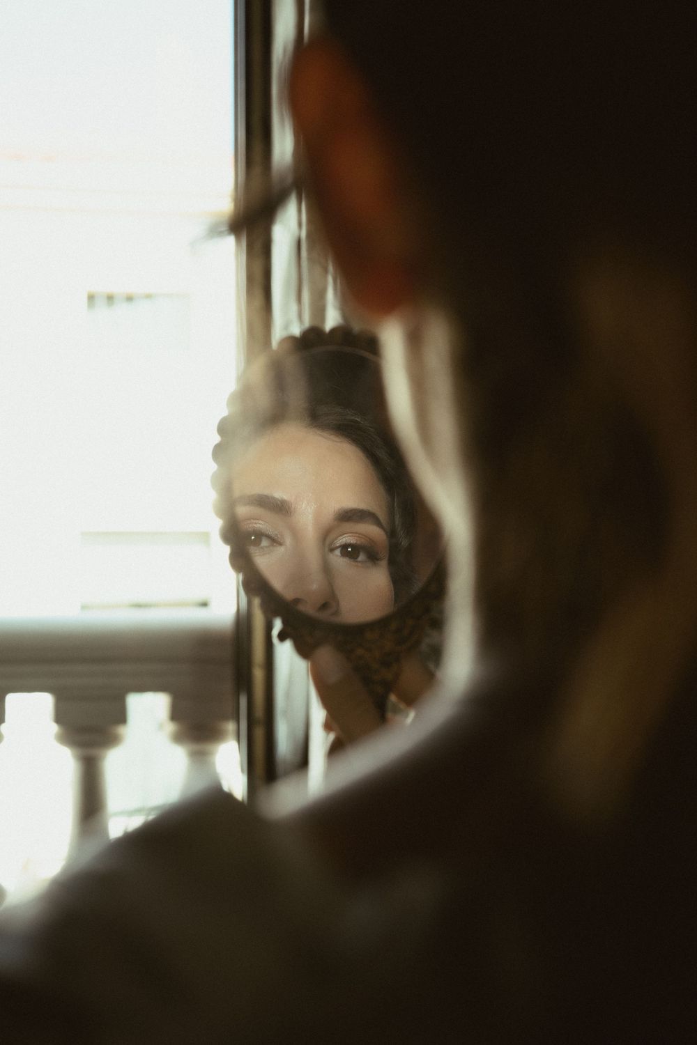 Artistic reflection in mirror shows soft window lighting and vintage decor elements creating moody ambiance.