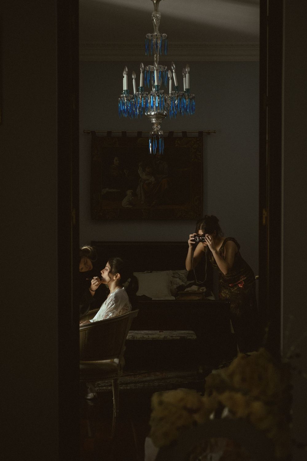 Two photographers take pictures in a dimly lit room beneath an elegant blue crystal chandelier.