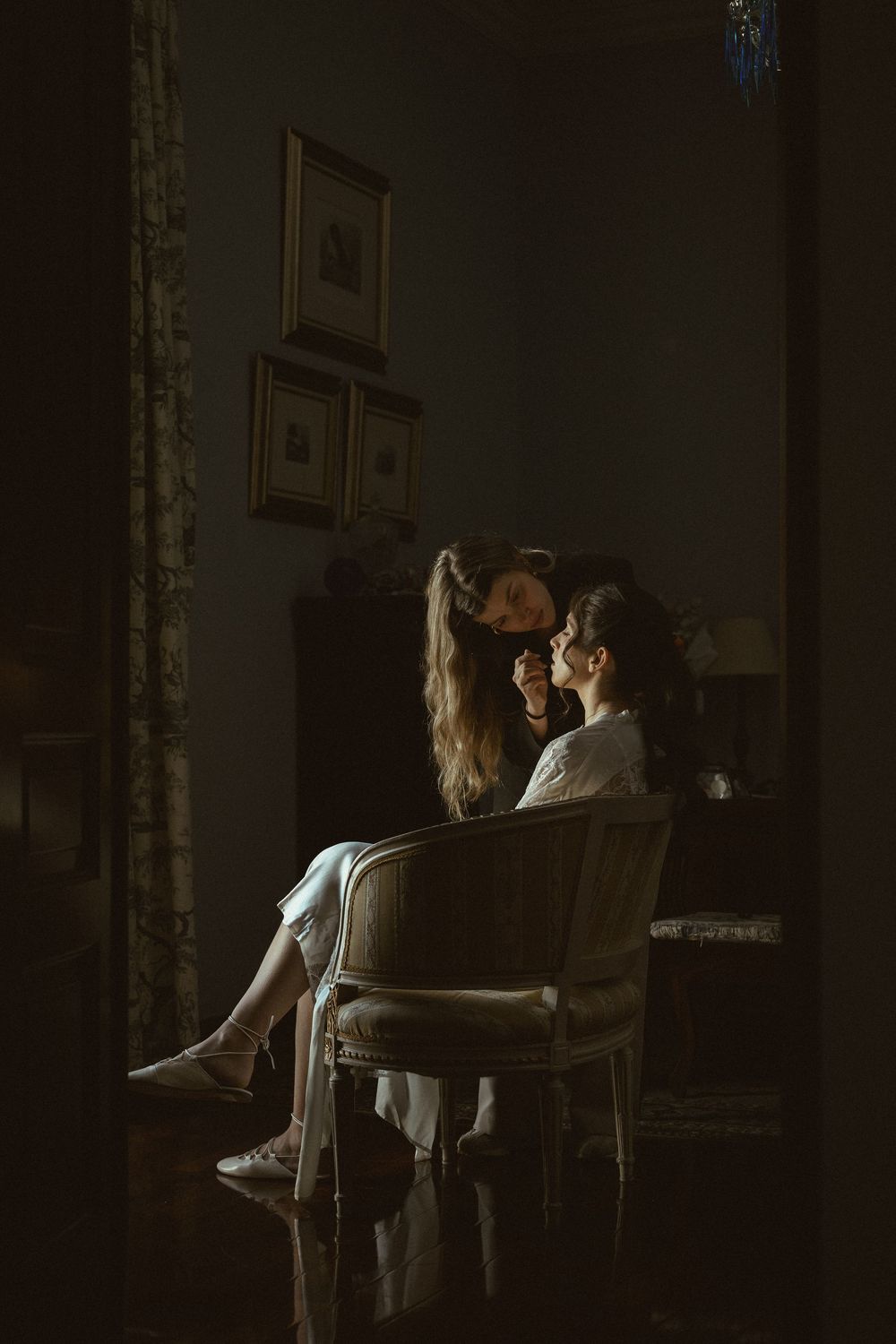 Moody dark interior scene with two figures in an intimate moment by a window.