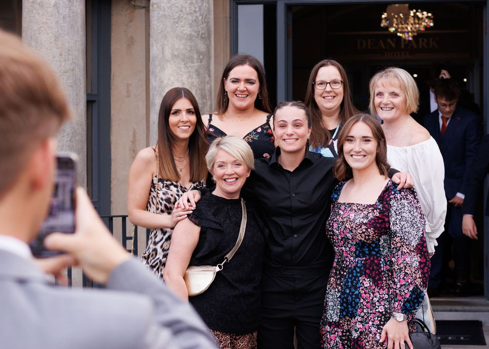 A group in formal attire poses together for a photo outside a building entrance.