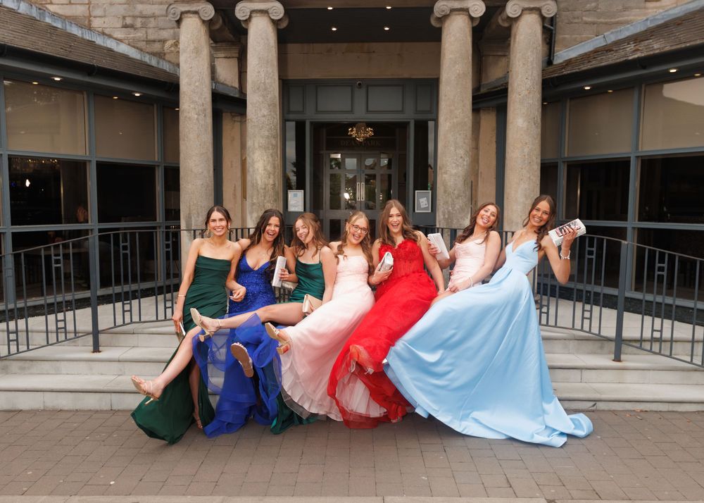 A group in elegant formal dresses pose together on stone steps of a building with classical columns.