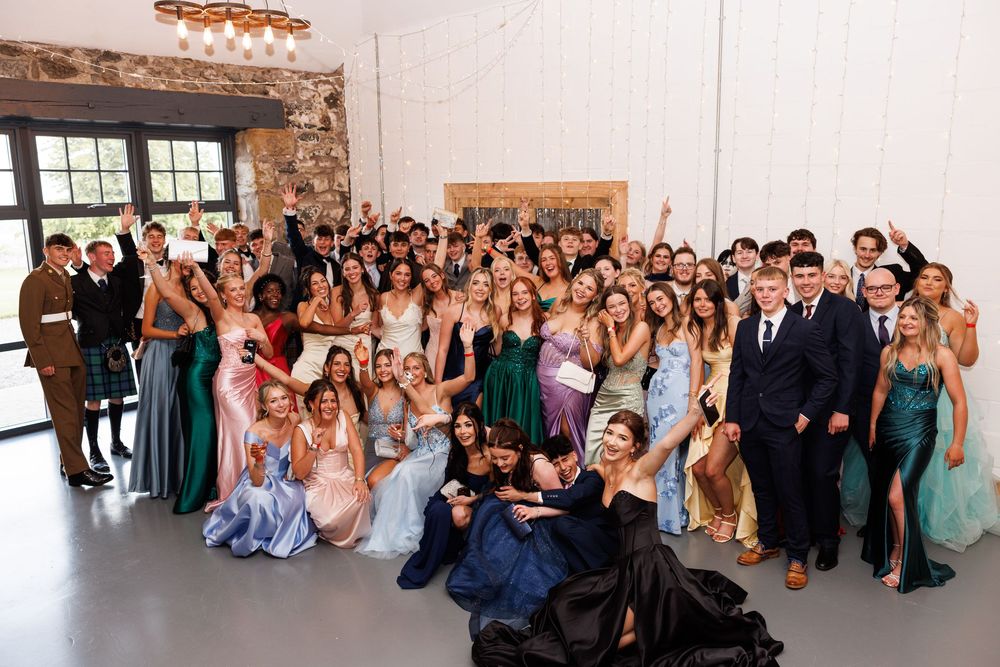 Large group of teenagers in formal attire posing together at prom, smiling and celebrating in an elegant venue.