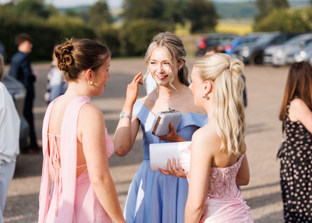 Three women in elegant pastel dresses chatting outdoors at a wedding reception on a sunny day.