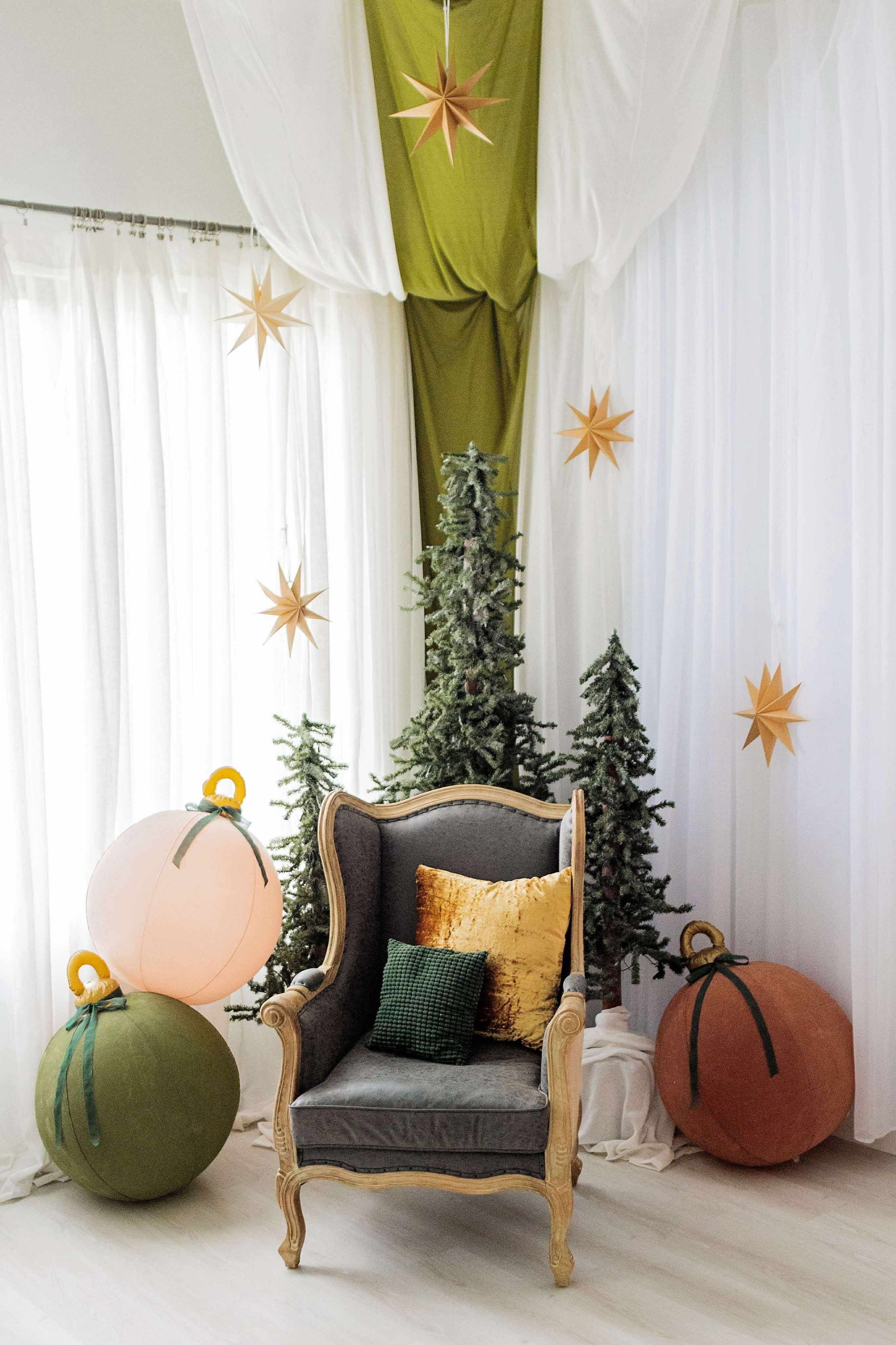 Elegant holiday corner with vintage gray armchair, fabric pumpkins, hanging gold stars and white drapes against green backdrop.