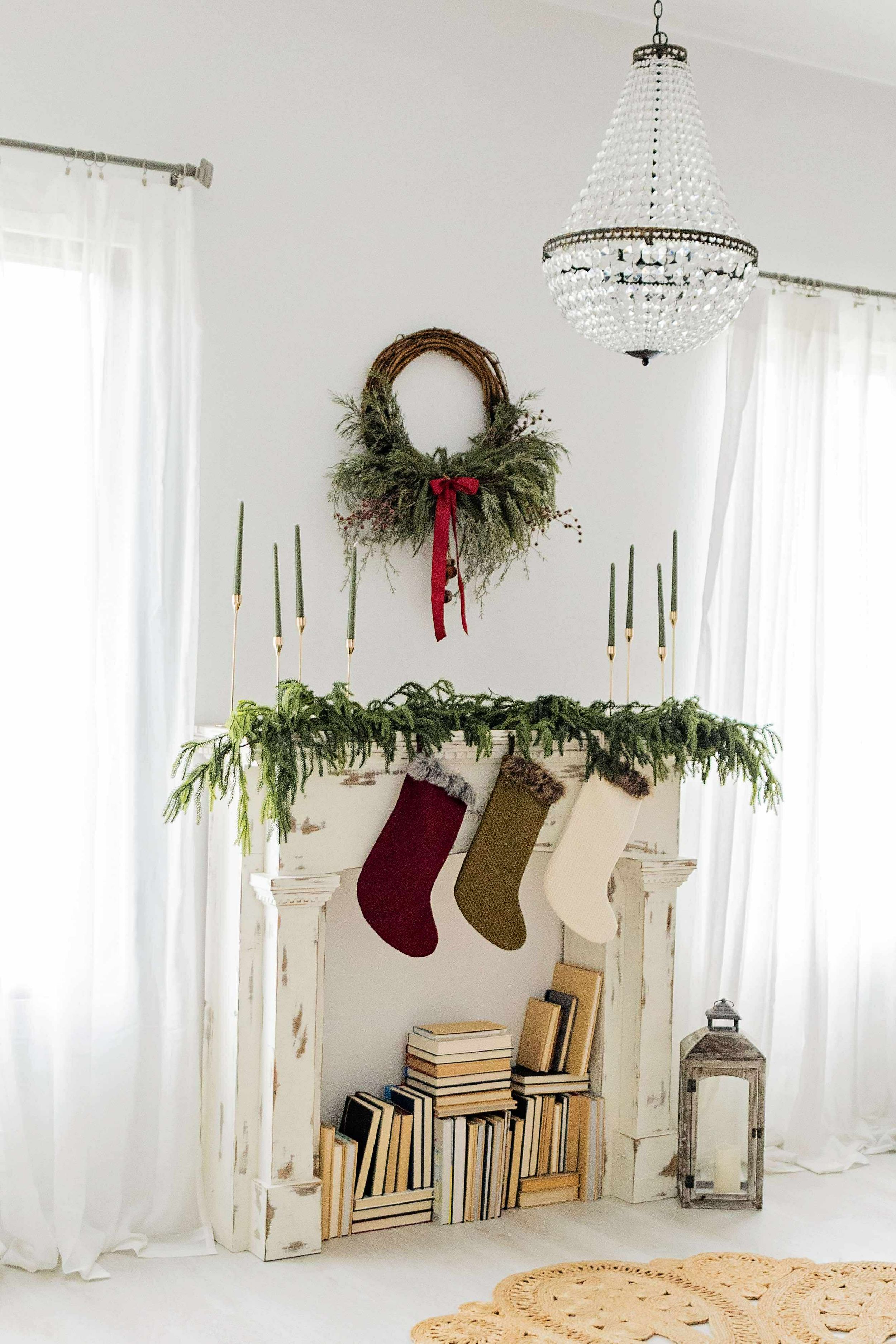 White minimalist living room interior with simple holiday decorations including hanging stockings and evergreen garlands.