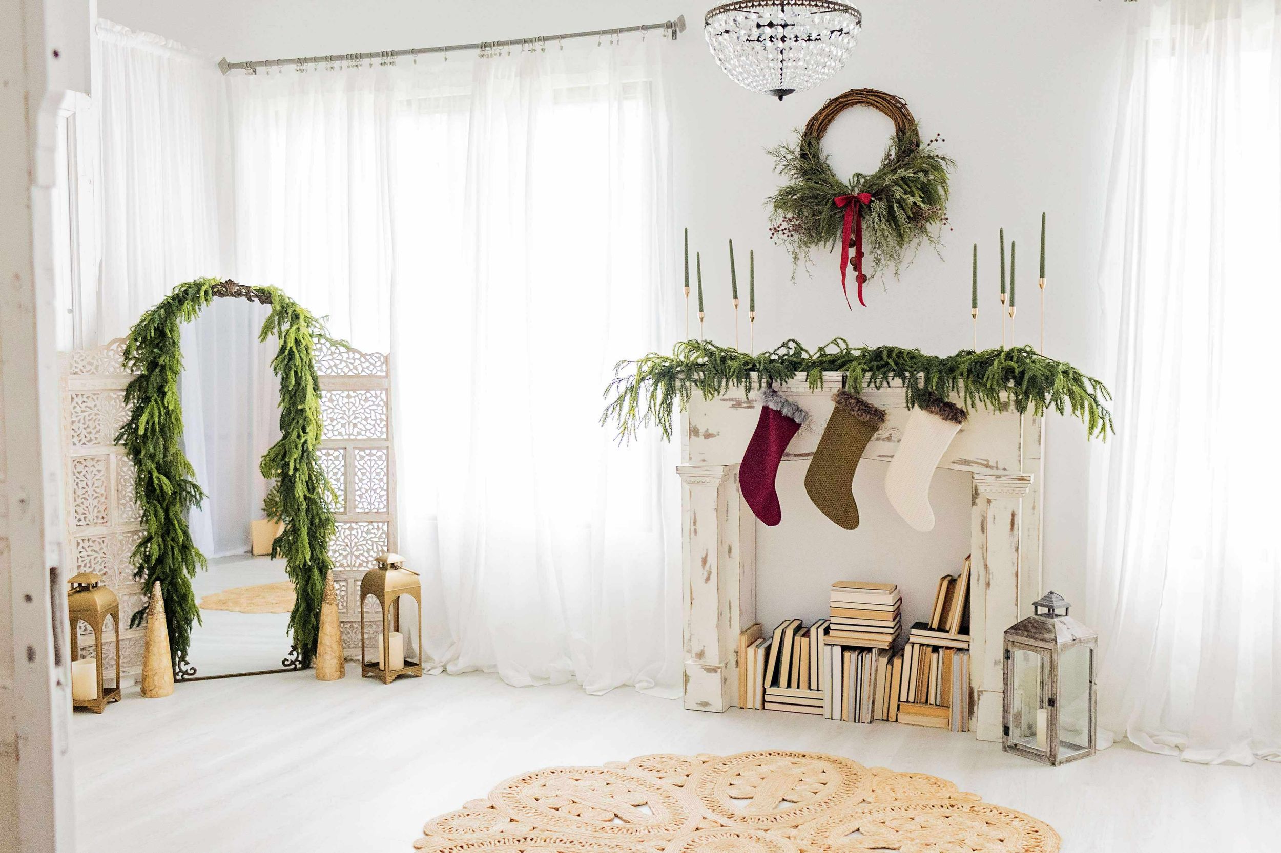 Minimalist white room decorated for Christmas with evergreen garland, stockings, a wreath and lanterns on the floor.
