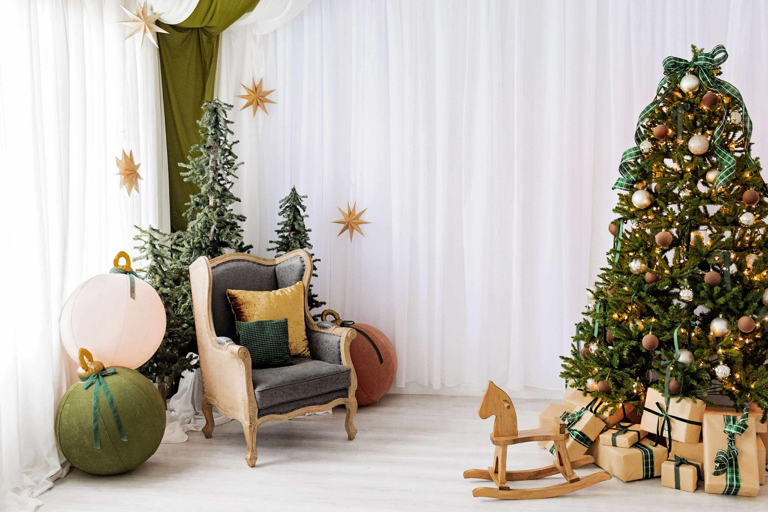 Modern white room with Christmas decor featuring a decorated tree, rocking horse, pumpkins, and a cozy armchair.
