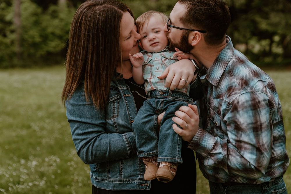 Happy young family with mother and father kissing their smiling toddler in a lush green park.