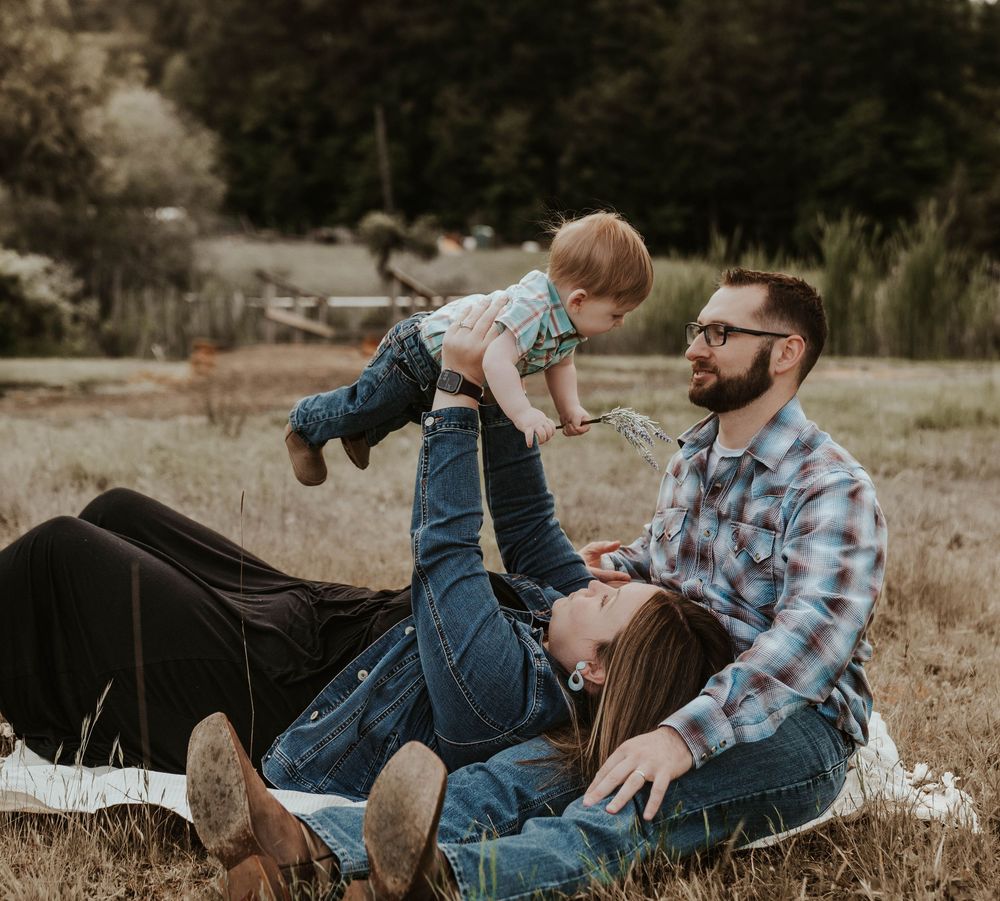 Family of three relaxing in a field with father lifting happy baby while mother lies in the grass.