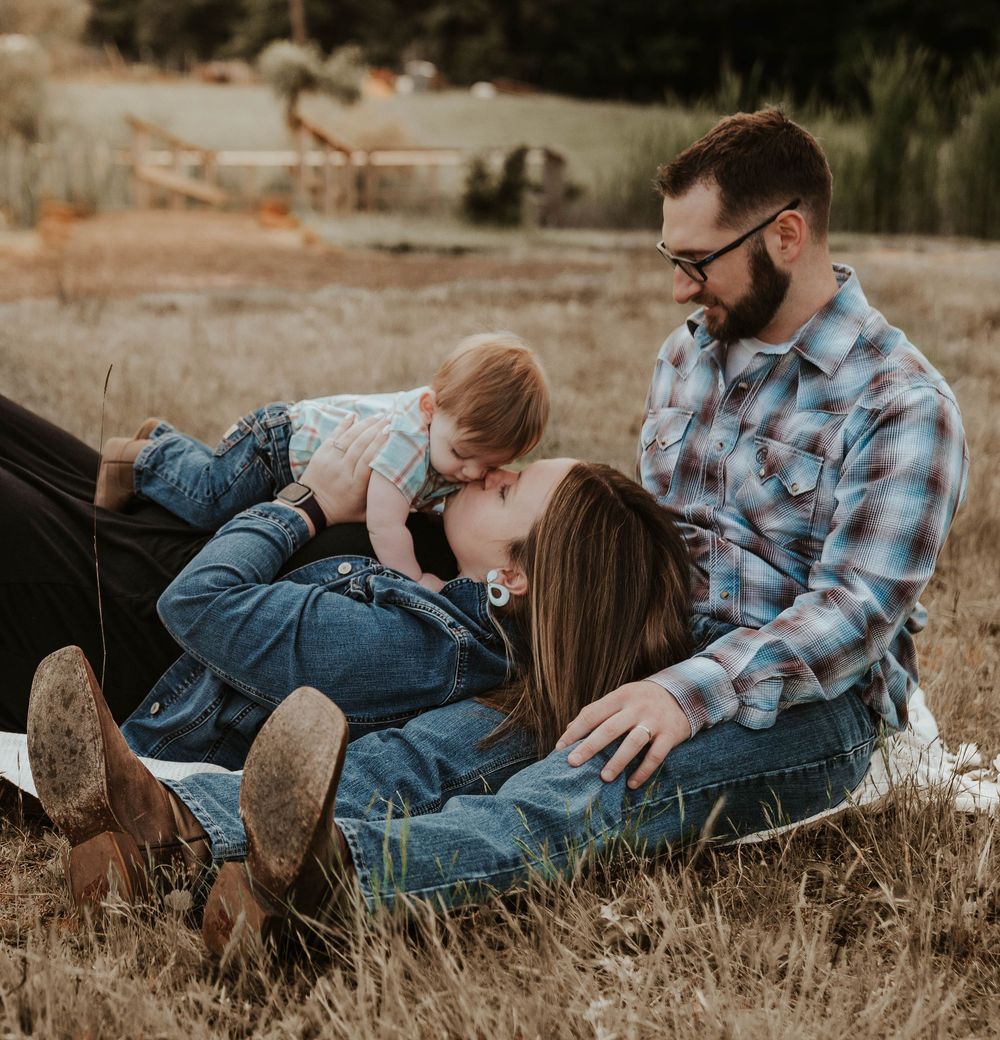 Loving family portrait of parents sitting in a golden field with their young toddler child.