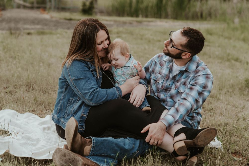 Young family sitting together in a grassy field sharing a joyful moment with their infant baby.