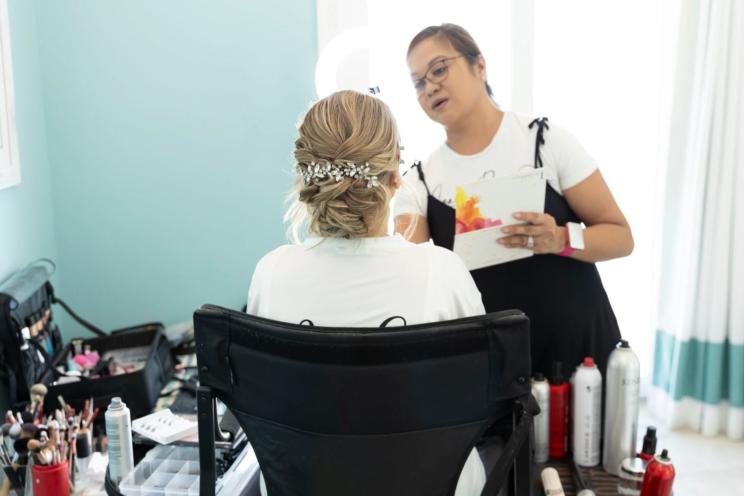 Professional makeup artist working with client in bright white studio with beauty supplies and tools.
